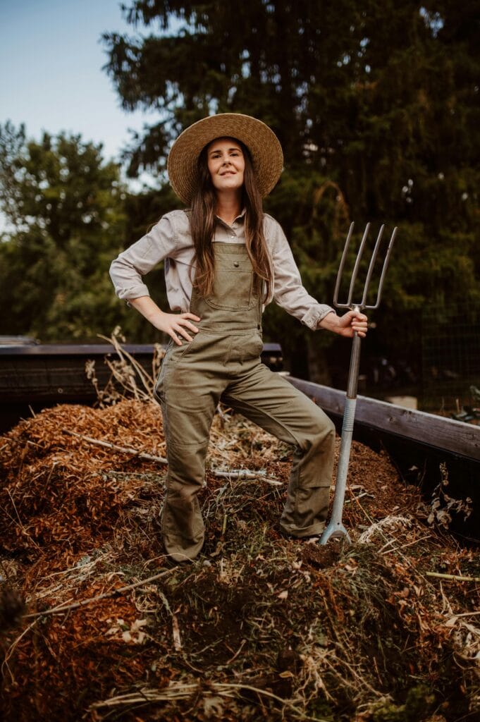 pexels-photo-28965889-28965889 Woman gardener proudly standing with pitchfork by a compost heap outdoors.